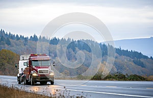 Big rig towing semi truck tow another semi truck on wet winding twilight autumn road in rain