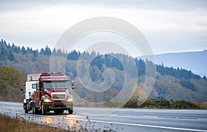 Big rig towing semi truck tow another semi truck on wet winding twilight autumn road in rain photo