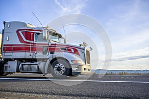 Big rig white bonnet semi truck tractor transporting cargo going on the local road