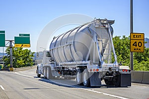 Big rig white day cab semi truck tractor transporting cargo in closed bulk semi trailer running on the highway exit intersection