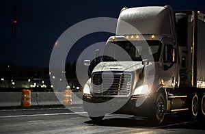 Big rig white day cab semi truck transporting cargo in semi truck driving on the wet rainy road in dark night time