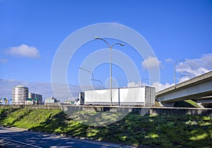 Big rig white day cab semi truck transporting goods in dry van semi trailer running on the highway entrance intersection