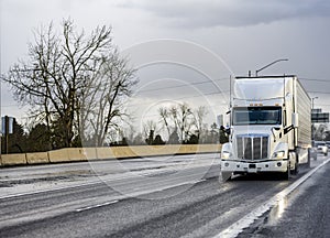 Big rig white industrial long haul semi truck transporting frozen cargo in refrigerator semi trailer running on the wide highway