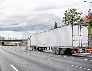 Big rig white long haul semi truck with dry van semi trailer running on the turning highway road with bridge ahead