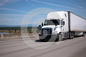 Big rig white semi truck with dry van trailer moving on wide straight highway