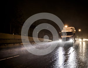 Big rig white semi truck transporting cargo in semitrailer driving on the night wet road with heavy rain and water dust