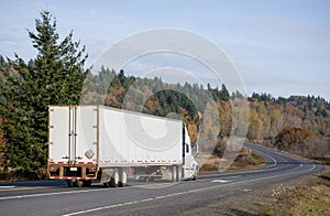 Big rig white semi truck transporting cargo in semi trailer with rusty back doors frame running on the winding road