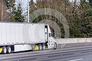 Big rig white semi truck transporting commercial cargo in dry van semi trailer driving on the straight wide highway road