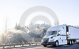 Bright white comfort ergonomic big rig semi truck with refregerated semi trailer running on winter highway wit frost hill photo