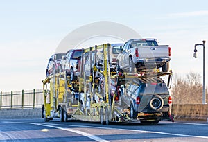 Big rig yellow car hauler semi truck transporting cars on two levels semi trailer driving on the overpass road