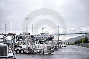 Big rigs car haulers semi trucks with loaded cars standing in row on the warehouse parking lot