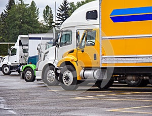 Big rigs semi trucks different makes and sizes standing in row on truck stop parking lot