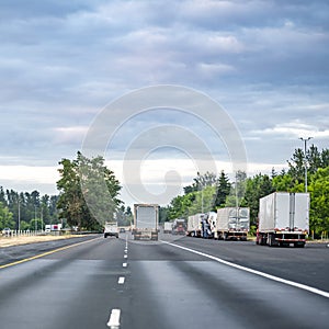 Big rigs semi trucks with different loaded semi trailers standing in a line by the side of the highway road for a break outside of