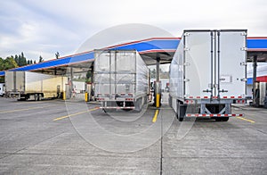 Big rigs semi trucks with different semi trailer standing on truck stop fuel station for refueling and continue delivering loaded