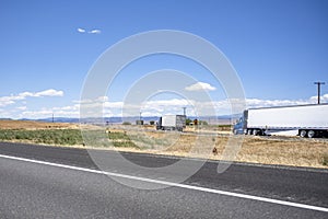 Big rigs semi trucks with different semi trailers standing on the highway exit road take a break according to the log book