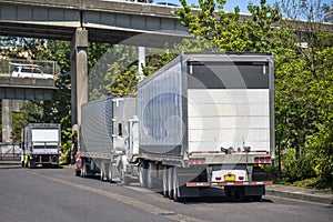 Big rigs semi trucks with dry van semi trailers parked on the street under overpass road intersection