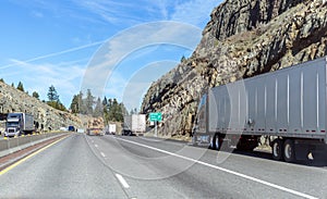 Big rigs semi trucks with loaded semi trailers running on mountain pass are moving along all lanes of the highway including along