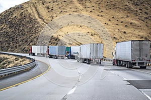 Big rigs semi trucks with loaded semi trailers slowly climbing uphill on the highway road to mountain pass in California