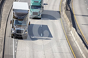 Big rigs semi trucks with semi trailers driving on merging road lines on wide highway