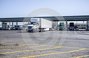 Big rigs semi trucks with semi trailers fill tanks with diesel at a fuel station on industrial truck stop