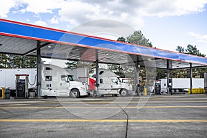 Big rigs semi trucks with semi trailers fuel trucks tanks with diesel on the truck stop gas station