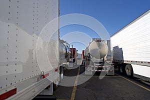 Big rigs semi trucks with semi trailers and round tanks standing