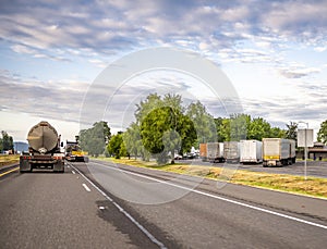 Big rigs semi trucks with semi trailers running on the road and standing for break on the rest area parking lot along the highway