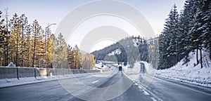 Big rigs semi trucks with semi trailers running toward each other on the divided winter highway road with exit with platform for