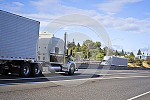 Big rigs semi trucks with semi trailers running towards each other in the opposite direction on the wide highway