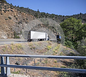 Big rigs semi trucks with semi trailers take a break standing on the road shoulder along the mountain river