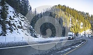 Big rigs semi trucks with semi trailers transporting cargo climbing in convoy on the winding winter highway road with snow and ice