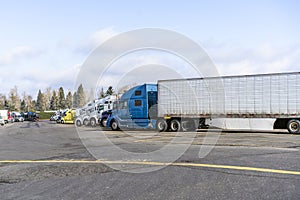 Big rigs semi trucks staing in row on wide truck stop parkink lot