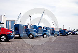 Big rigs semi trucks standing in row on huge parking lot at industrial area