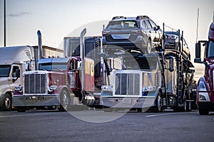 Big rigs semi trucks tractors with car hauler and refrigerator and dry van semi trailers standing in row on the truck stop