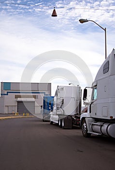 Big rigs semi trucks tractors stand in a row on the roadside in