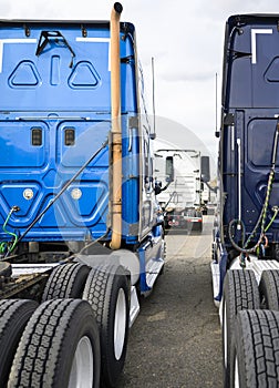 Big rigs semi trucks tractors standing in row on the parking lot waiting for loaded semi trailer for next delivery