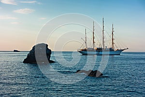 Big rock and sailing ship at sunset in front of city harbor, Skopelos island