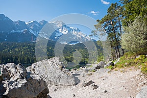 big rocks at lake shore Eibsee, stunning view to Zugspitze mountain, pine trees beside