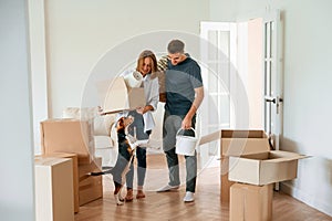 In the big room, with boxes in hands. Young couple with dog are moving to new home