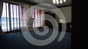 Big room with large windows, tables and arm-chairs and blue carpet. Modern hotel room view