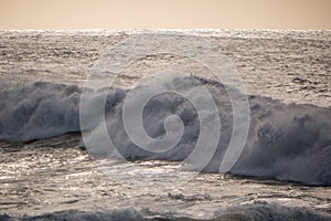 Big, rough white wave breaking on sea at dusk with soft golden light