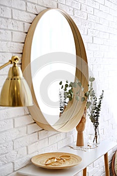 Big round mirror, table with jewelry and decor near brick wall