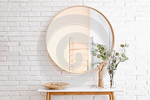 Big round mirror, table with jewelry and decor near brick wall in hallway