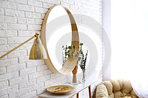 Big round mirror, table with jewelry and decor near brick wall in hallway interior