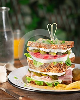 Big sandwich with ham, salami, pickled cucumbers, fresh cheese and lettuce on a rustic table, served with French fries. Space for