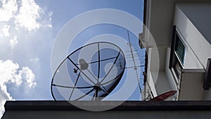 Big Satellite Dish, small red Satellite Dish and Antenna TV on the roof of house against with blue sky and white clouds