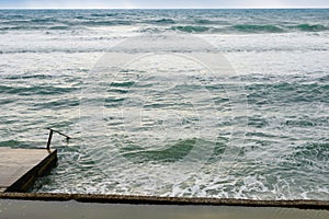 Big sea waves breaking on concrete pier in windy weather