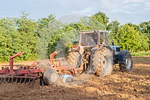 Big silver tractor with a red harrow disc cultivator in the field on a sunny day. The concept of work in a fields and agricultur photo