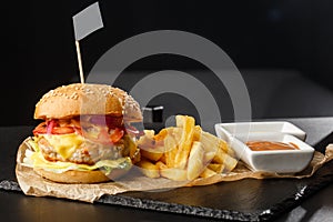 Big single chickenburger with french fries isolated on black background. hamburger with chicken patty , onion, tomato, lettuce