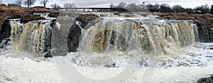 The Big Sioux River flows over rocks in Sioux Falls South Dakota with views of wildlife, ruins, park paths, train track bridge, tr